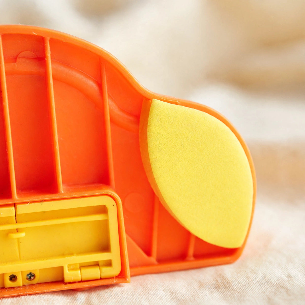 Close-up of the underside of the yellow duck treat dispenser showing its orange ribbed body, a yellow anti-slip felt pad, and a yellow compartment door.