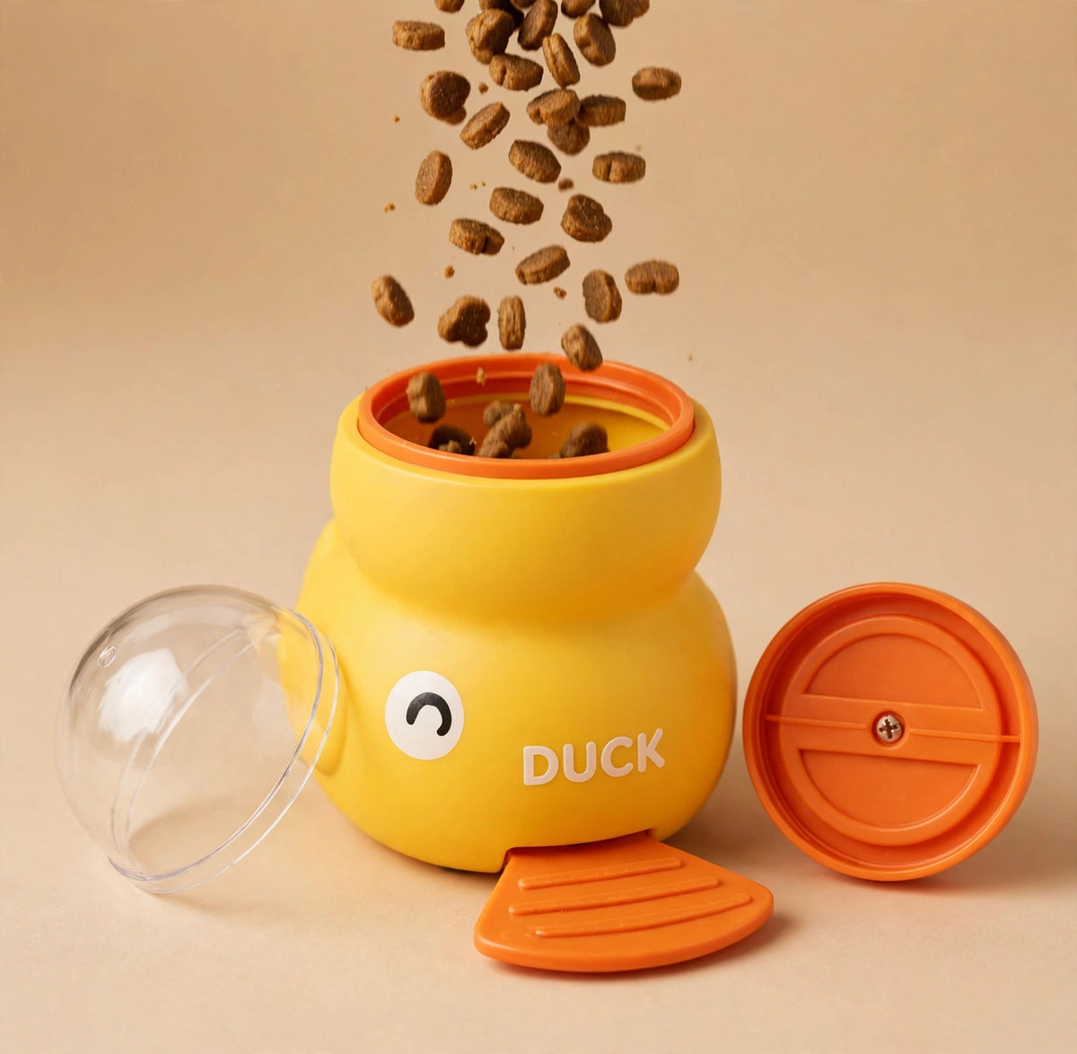 Kibble falling into the open top of the yellow duck treat dispenser, with its transparent dome lid and orange twist lid lying beside it.