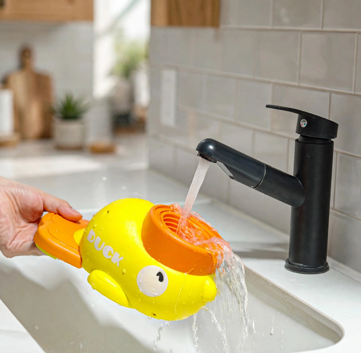 A hand rinsing the yellow duck treat dispenser under a black kitchen faucet.