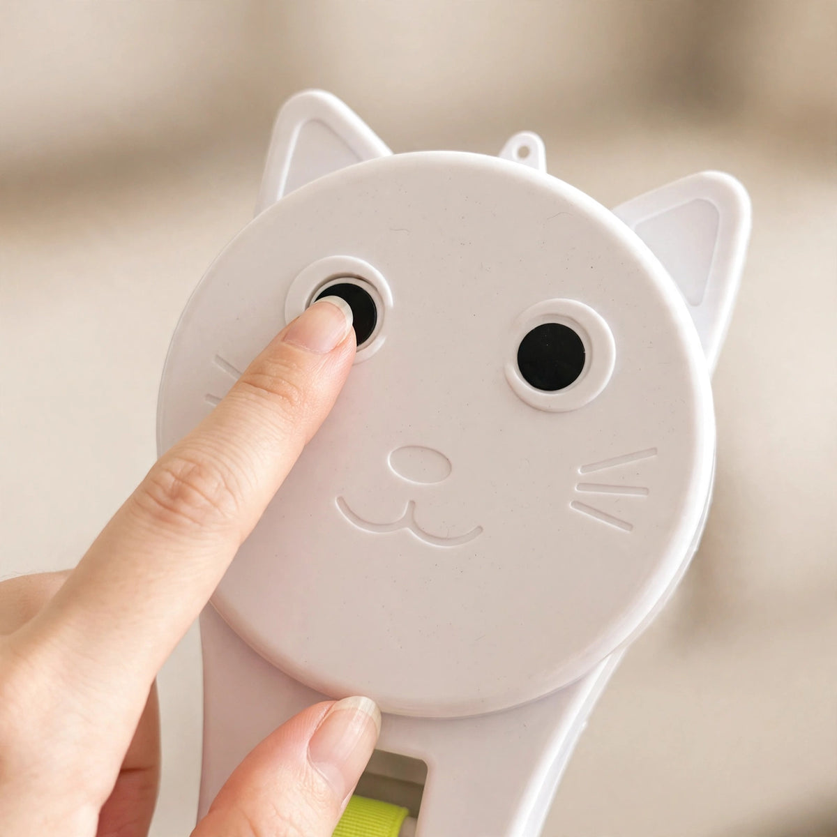 Close-up of a finger pressing the cat-eye button on the white cat-face-shaped teaser device.