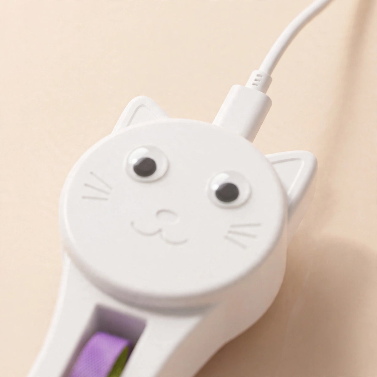 Close-up of the white cat-face-shaped teaser with a white USB-C charging cable plugged into its Type-C charging port.