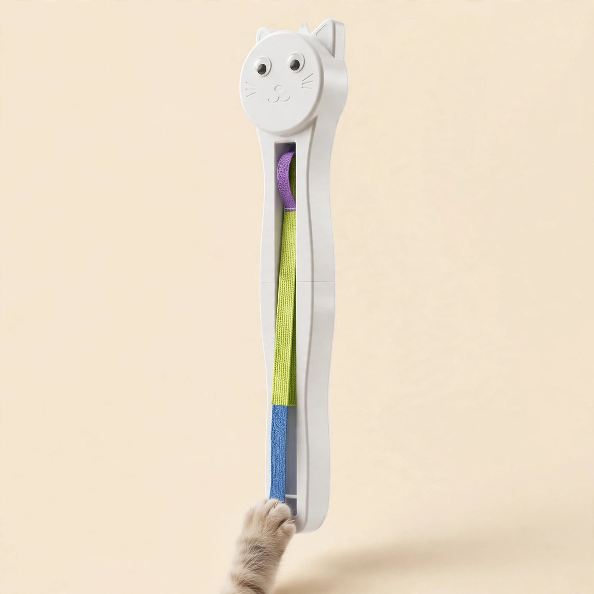White cat-face-shaped wall-mount cat teaser with a long flat woven strap in purple, yellow-green, and blue segments, as a cat's paw reaches up to touch it.