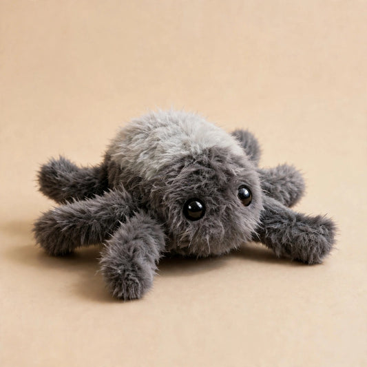 Gray fluffy plush spider cat toy with large black eyes resting on a beige background.