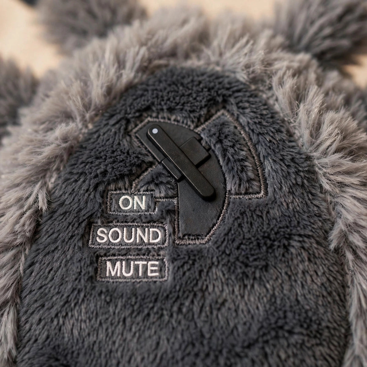 Close-up of the gray plush spider toy's three-position switch with embroidered labels ON, SOUND, and MUTE.