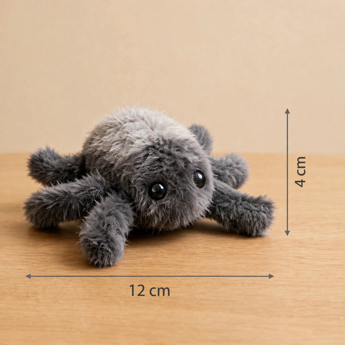 Gray plush spider toy on a wooden surface with dimension markings showing 12 cm wide and 4 cm tall.